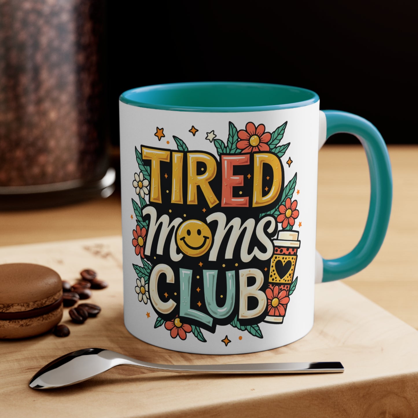White mug with teal handle and "Tired Moms Club" text and graphics.