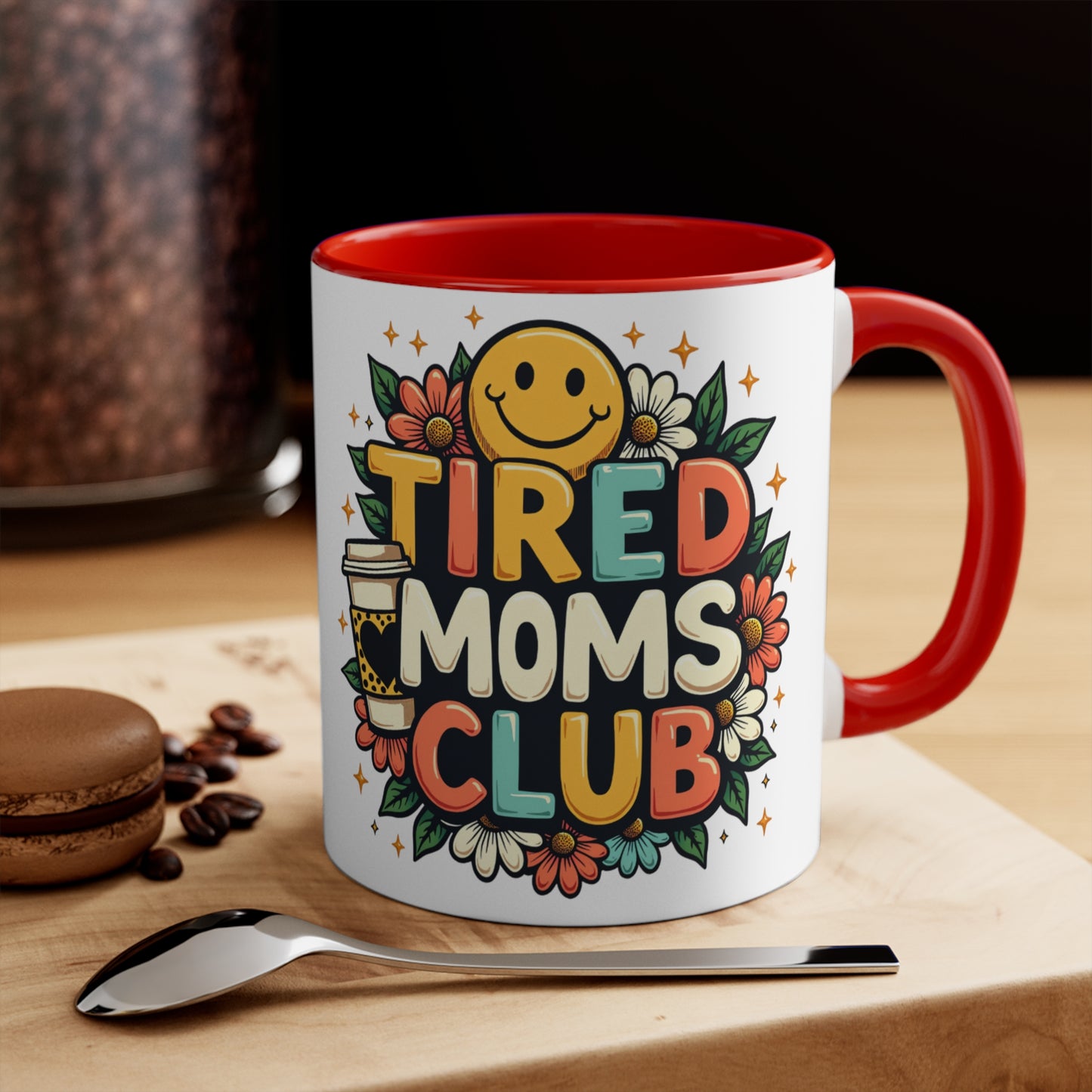 White mug with "Tired Moms Club" text, smiling face, coffee cup, and flowers.