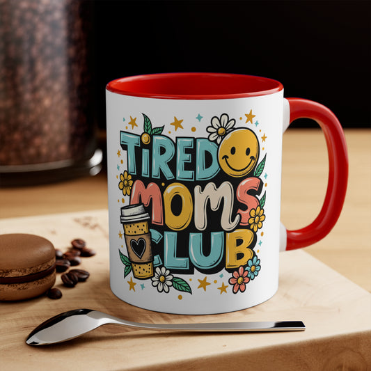 White mug with "Tired Moms Club" design, red interior, and coffee beans.