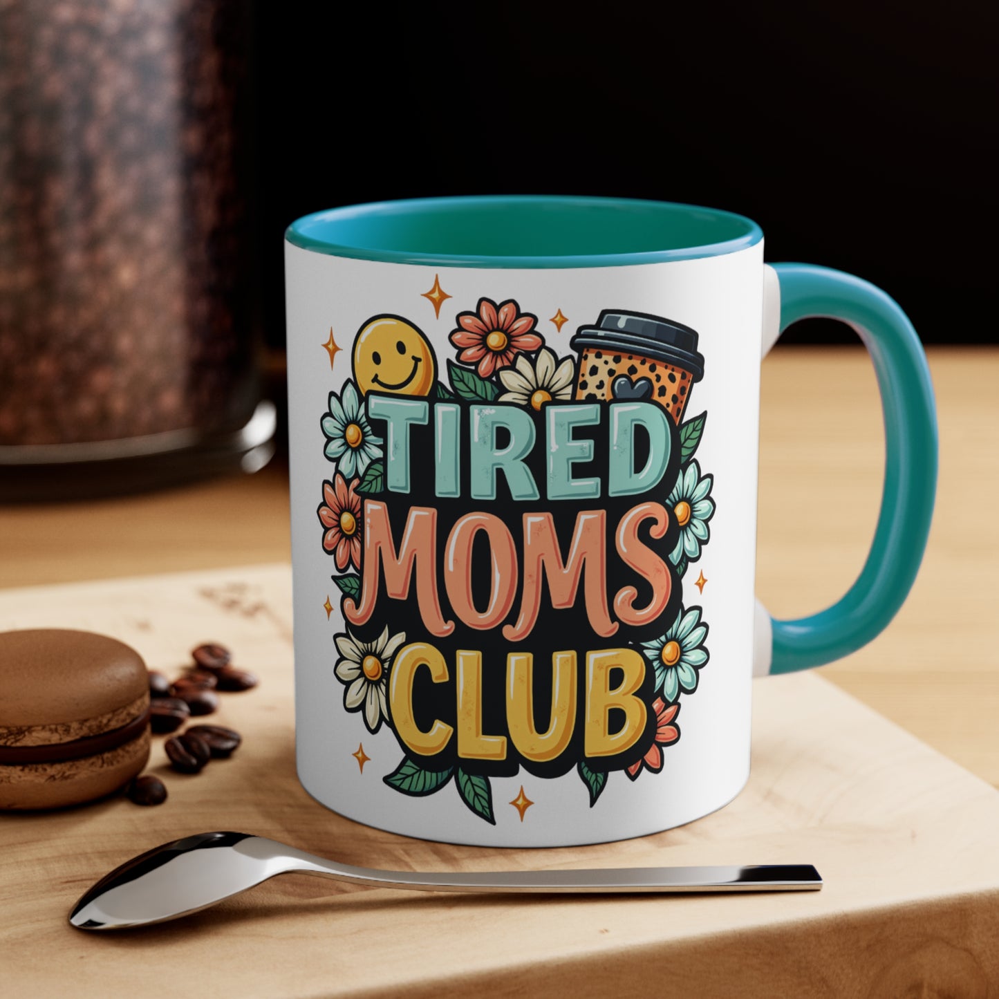 White mug with "Tired Moms Club" in colorful text and floral graphics.