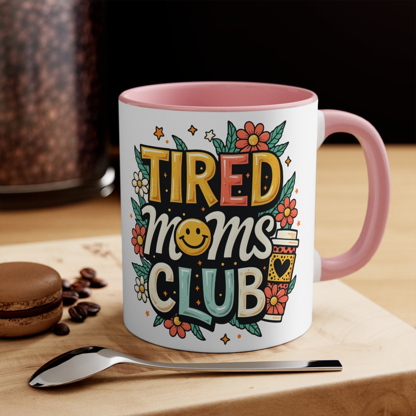 Mug with "Tired Moms Club" text, smiling face, coffee cup, and flowers.
