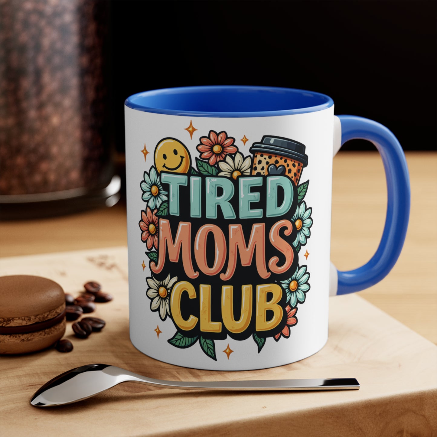 White mug with blue handle, "Tired Moms Club" text and floral design.